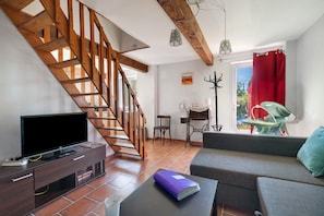 Ein Wohnzimmer mit einer Holztreppe, einem Fernseher, einer Couch und einem Esstisch.
