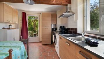 A compact kitchen with wooden cabinets, a built-in washing machine, and a window with a view of greenery.