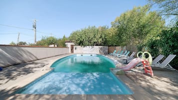 A swimming pool with a slide, surrounded by lounge chairs and a brick wall.