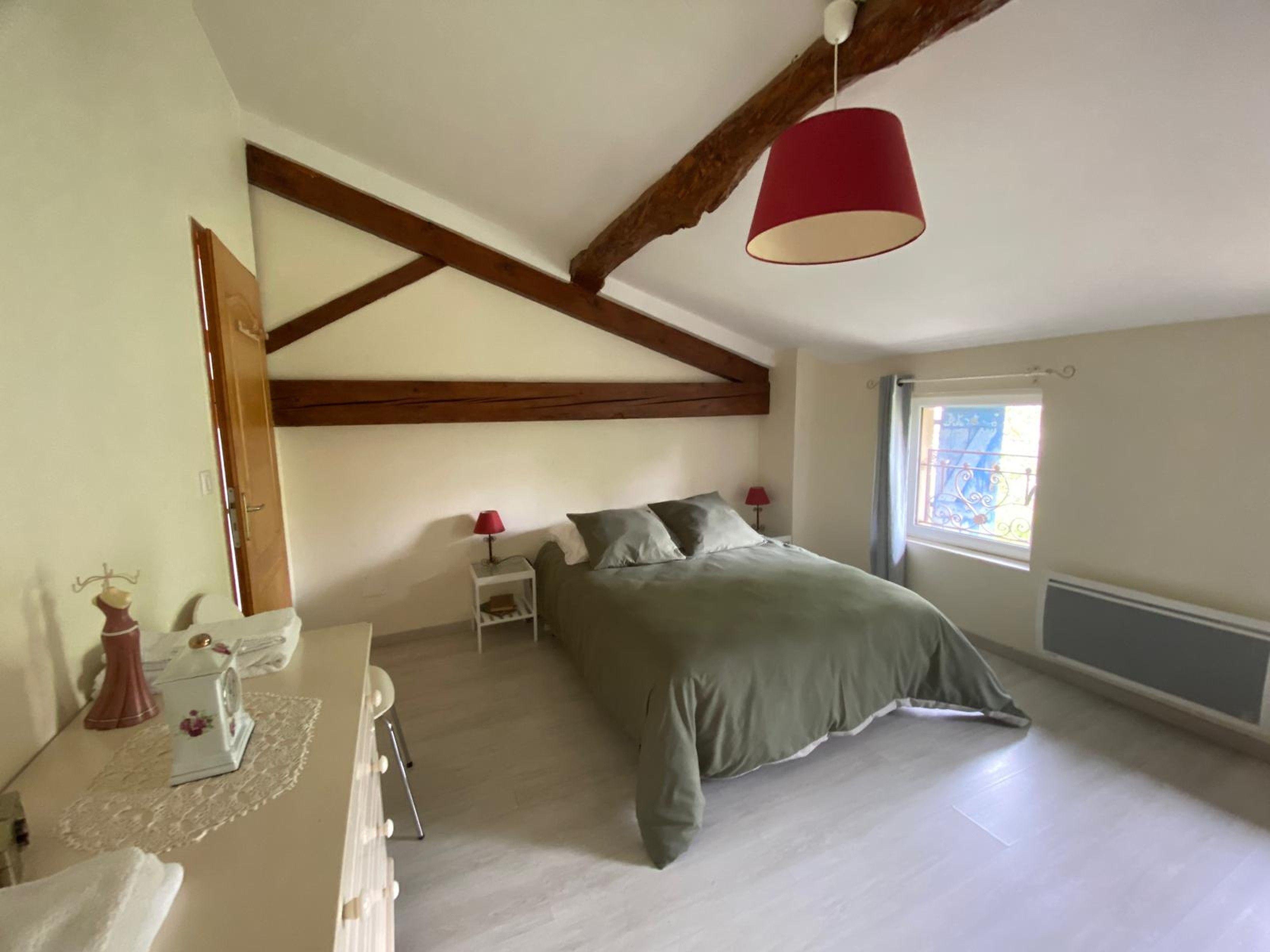 Un dormitorio con una cama, cómoda, mesita de noche, lámpara y ventana con cortinas.