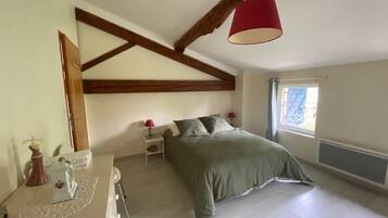 Un dormitorio con una cama, cómoda, mesita de noche, lámpara y ventana con cortinas.