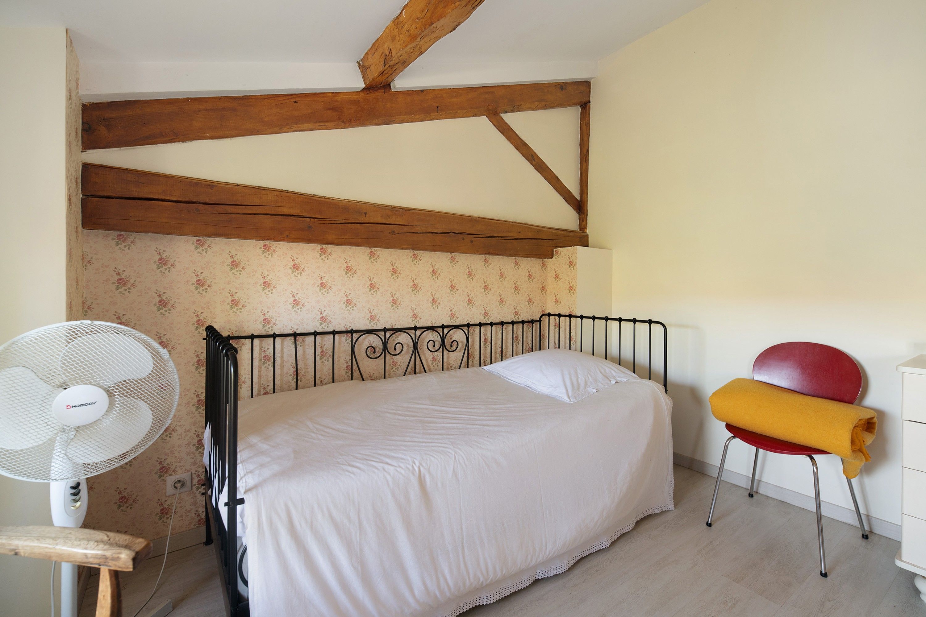 Une chambre à coucher avec un lit, un ventilateur, une chaise et une commode.