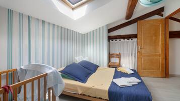 Un dormitorio con tragaluces, una cama con ropa de cama azul, una cuna de madera y una puerta.