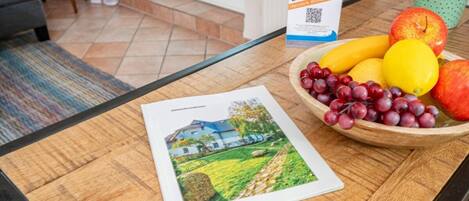 Une brochure posée sur une table, à côté d’un panier de fruits, d’un panneau et d’une photo d’une maison.
