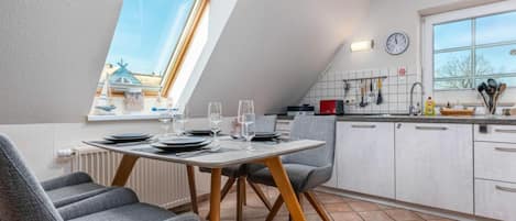 Una cocina moderna con zona de comedor, que incluye una mesa preparada para cuatro personas, un ventanal con vistas y un reloj en la pared.