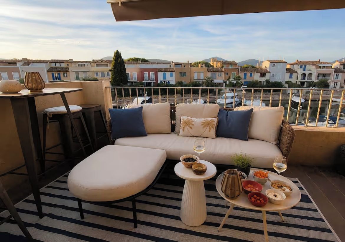 Ein Balkon mit einer Couch, einem kleinen Tisch und einem Esstisch, gedeckt mit Speisen und Getränken.
