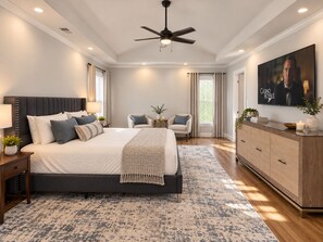 Un dormitorio con una cama grande, ventilador de techo, televisor y cómoda de madera.
