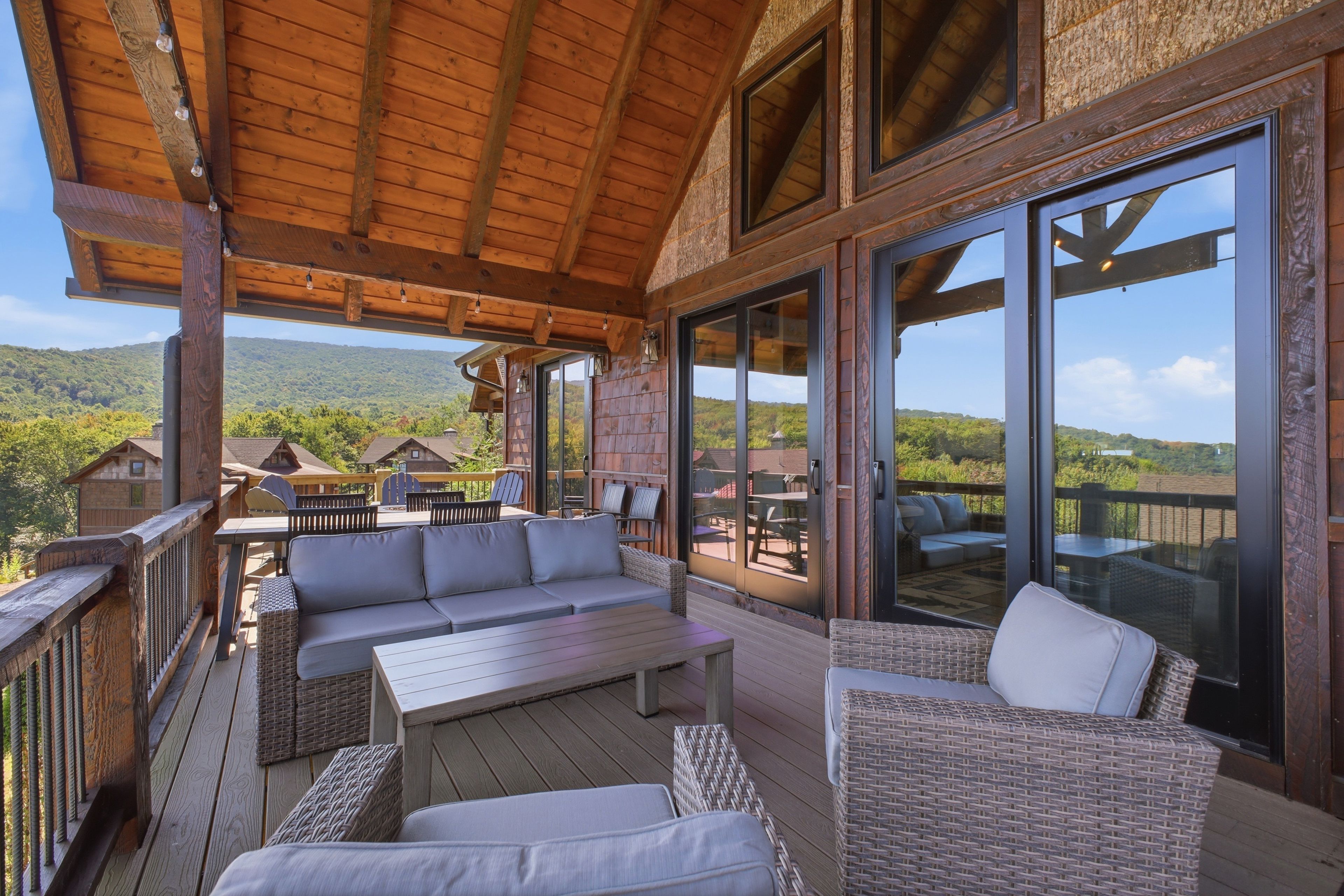 Ein überdachter Außenbereich mit Korbmöbeln und einer Holzterrasse, mit Blick auf eine gebirgige Landschaft.