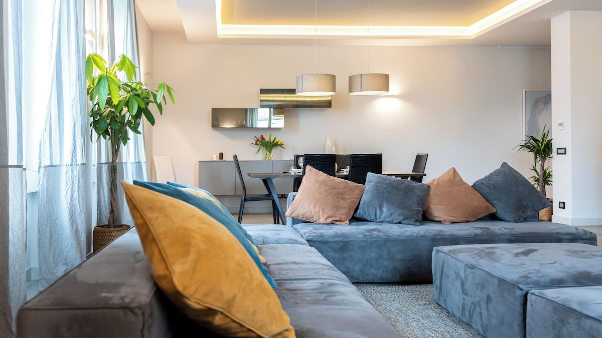 Ein modernes Wohnzimmer mit einer Eckcouch, einem Essbereich und einer Küche im Hintergrund.