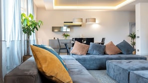 Una sala moderna con un sofá modular, un comedor y una cocina al fondo.