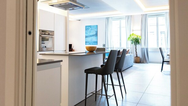Una cocina moderna con una isla central, taburetes de bar y un comedor con un ventanal grande.