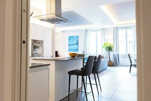 Una cocina moderna con una isla central, taburetes de bar y un comedor con un ventanal grande.