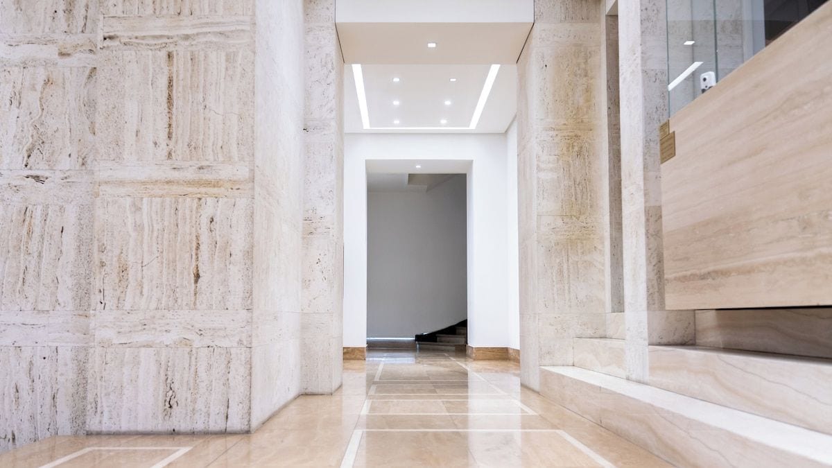 A modern interior with a marble floor, a staircase, and a wooden reception desk.