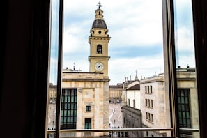 Vista de un edificio histórico con una imponente torre del reloj, a través de una ventana con marco de metal.