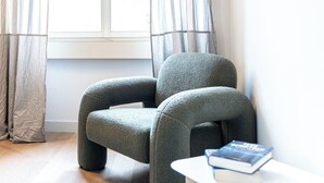 Una habitación con un sillón gris y una mesita con un libro.