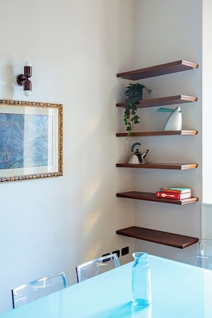 A room with a white table, a framed artwork, and wooden shelves with books and a plant. - Downtown Milan FamilySuite | 6 beds w/ workspace (Milano)