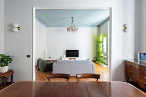 A dining area with a wooden table and chairs, a television in the background, and a bookshelf with green and white books. - Downtown Milan FamilySuite | 6 beds w/ workspace (Milano)