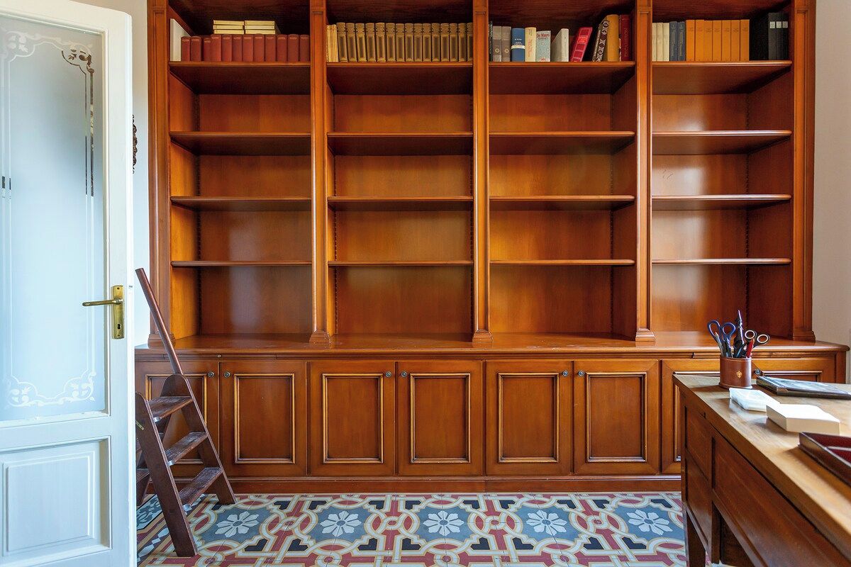 Ein Bücherregal aus Holz mit mehreren Einlegeböcken, ein Schreibtisch mit Stuhl und ein fußboden mit Muster.