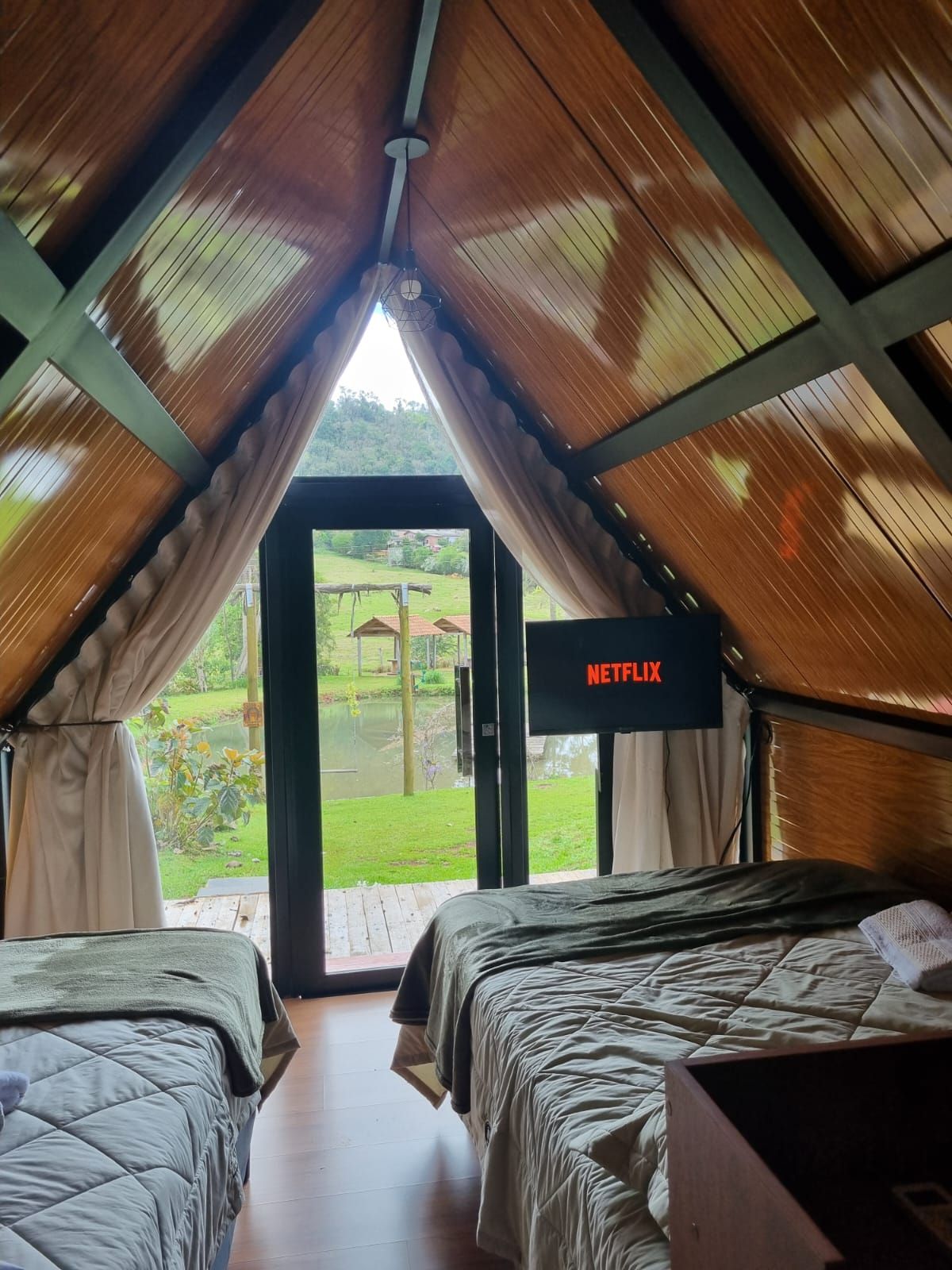 A room with two beds, a television displaying 'NETFLIX,' and a view of a garden through a door.