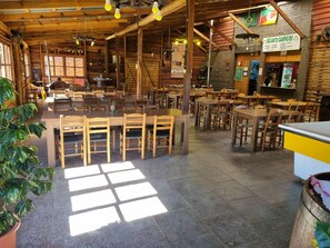 Un interior rústico de madera con varias mesas y sillas, una zona de bar y un tablero de menú visible.