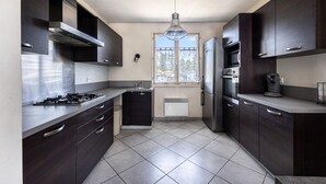A modern kitchen with dark cabinetry, a gas stove, a built-in oven, and a refrigerator. - L’Écrin de Cussac - proche commerces (Cussac)