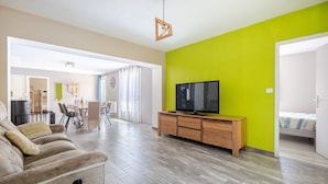 A modern living room with a sofa, a TV on a wooden cabinet, and a dining area in the background. - L’Écrin de Cussac - proche commerces (Cussac)