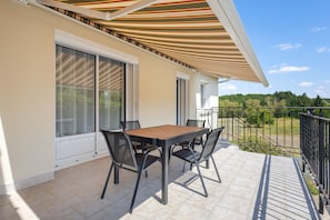 Ein Balkon mit Tisch und Stühlen, eine hölzerne Pergola und Blick auf die umliegende Landschaft.