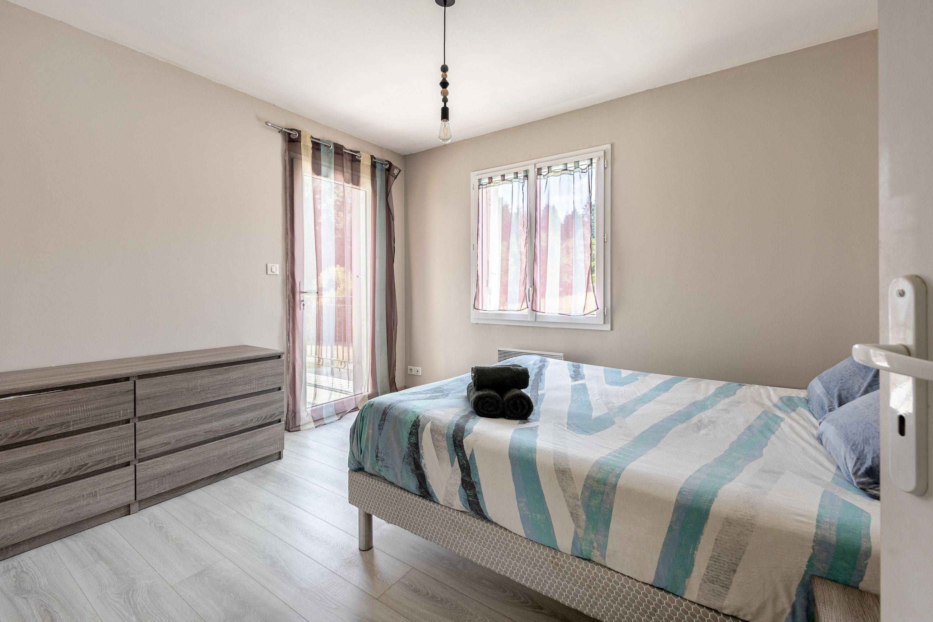 Quarto com cama, penteadeira e janela com cortinas.