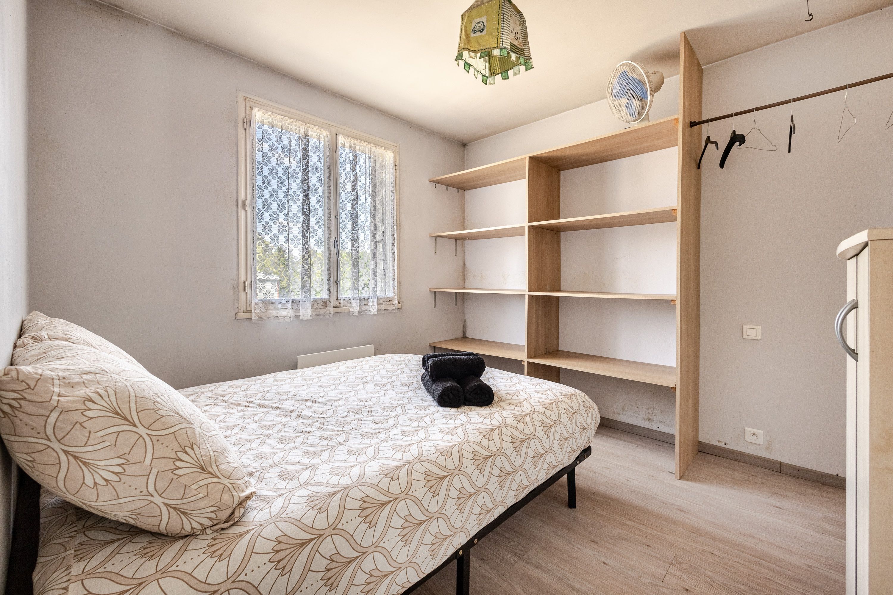 Ein Schlafzimmer mit Bett, einem Fenster mit Vorhängen, einem Kleiderschrank und einer Pendelleuchte.
