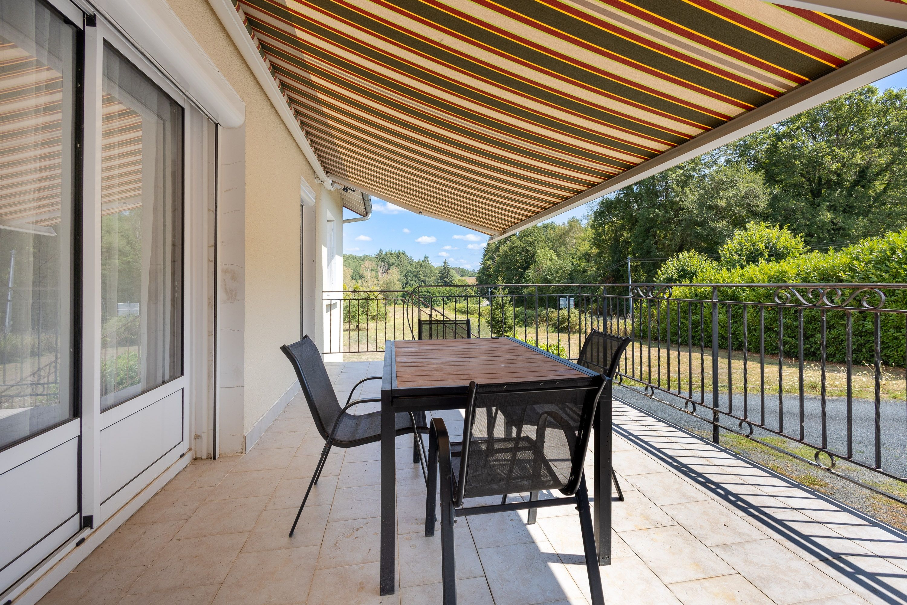 Alpendre coberto com mesa, cadeiras, guarda-corpo e vista para o verde.