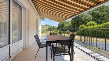 Alpendre coberto com mesa, cadeiras, guarda-corpo e vista para o verde.