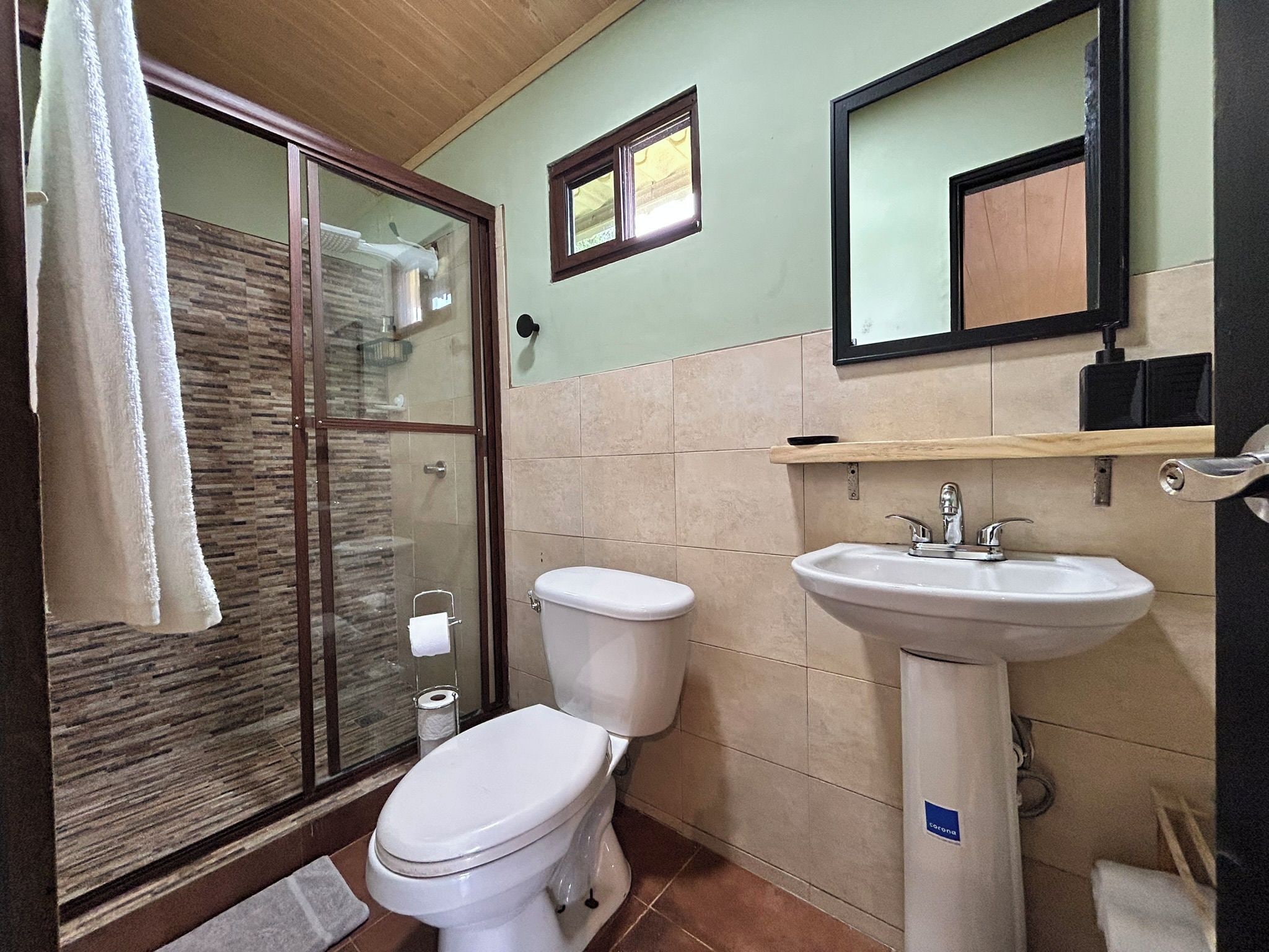 A bathroom with a glass shower enclosure, a toilet, and a sink.