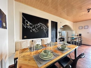 A dining area with a wooden table set for four, a black wall art of a map, and a kitchen in the background. - Mountain Cabin with a View of Barú Volcano (Jaramillo)