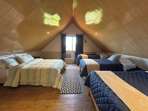 A triangular attic bedroom with three beds arranged in a U-shape, wooden floors, and a window with curtains. - Mountain Cabin with a View of Barú Volcano (Jaramillo)