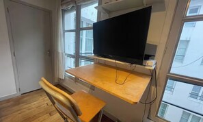 Une pièce comprenant un bureau en bois, une chaise et un téléviseur fixé au mur.