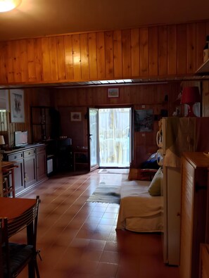 Interior de una cabaña con paredes de madera, una zona de cocina, una mesa de comedor y un sofá.