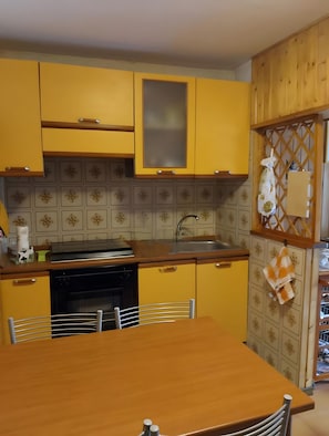 Cuina amb armaris grocs, una taula de fusta i un rentaplat.