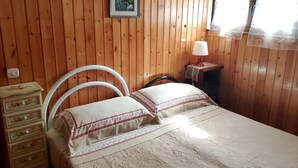 A wooden-paneled room with a bed, a dresser, a lamp, and a framed picture on the wall.
