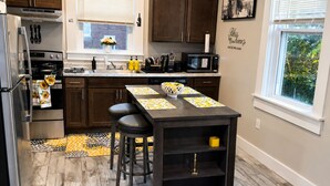 A modern kitchen with dark wooden cabinets, a stainless steel refrigerator, a built-in oven, and a microwave. There is a window with blinds, a sink with a faucet, and a vase with flowers on the counter. - Adorable 2-bedroom apartment with AC in charming Norwood (Norwood)