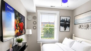 A bedroom with a bed, a TV, a ceiling fan, a window with blinds, and artwork on the walls. - Adorable 2-bedroom apartment with AC in charming Norwood (Norwood)