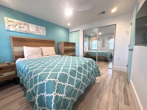 Ein Schlafzimmer mit einem Bett, einem Holz-Kopfteil, einem Schminktisch, einem Spiegel und einer Tür zu einem anderen Raum.