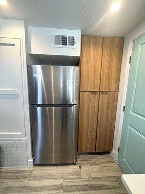 A stainless steel refrigerator and wooden cabinets in a kitchen with a light blue door and a vent on the wall. -  APARTMENT in Paradise / Cozy 1-Bedroom / Steps to Madeira Beach! (Madeira Beach)