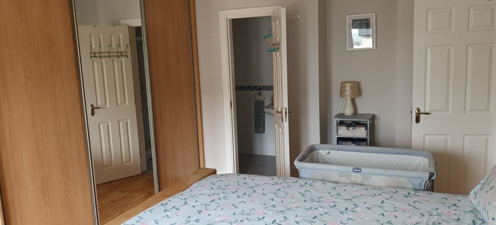 A bedroom with a bed, a wardrobe, a mirror, and a small bedside table with a lamp.