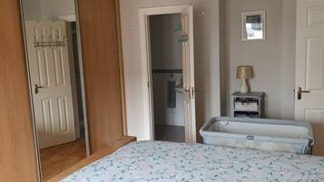 A bedroom with a bed, a wardrobe, a mirror, and a small bedside table with a lamp.