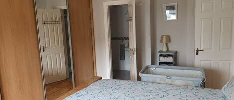 A bedroom with a bed, a wardrobe, a mirror, and a small bedside table with a lamp.