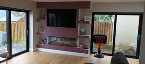 A living room with a fireplace, a television mounted on the wall, and a basketball hoop. - 4 bedroom house in Athenry town on the grounds of the 4 Star Raheen Woods hotel (Athenry)
