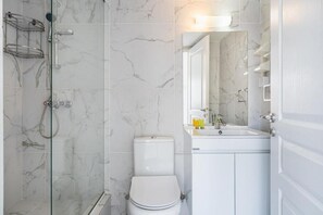 Un baño con cabina de ducha de vidrio, inodoro blanco y lavabo con espejo.