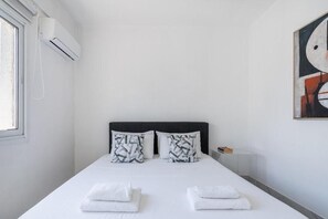 Ein Hotelzimmer mit Bett, Kissen, einem Nachttisch, einer Klimaanlage und einem Bild an der Wand.