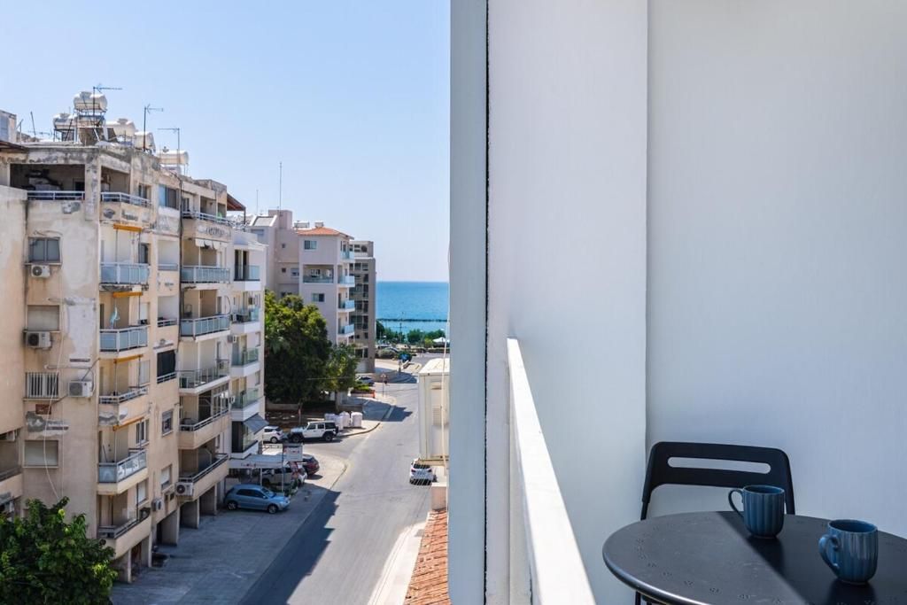 A balcony with a view of a street and buildings, a table with two chairs, and a clear sky.