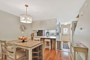 Cozinha moderna com armários brancos, mesa de jantar de madeira e luminária pendente.